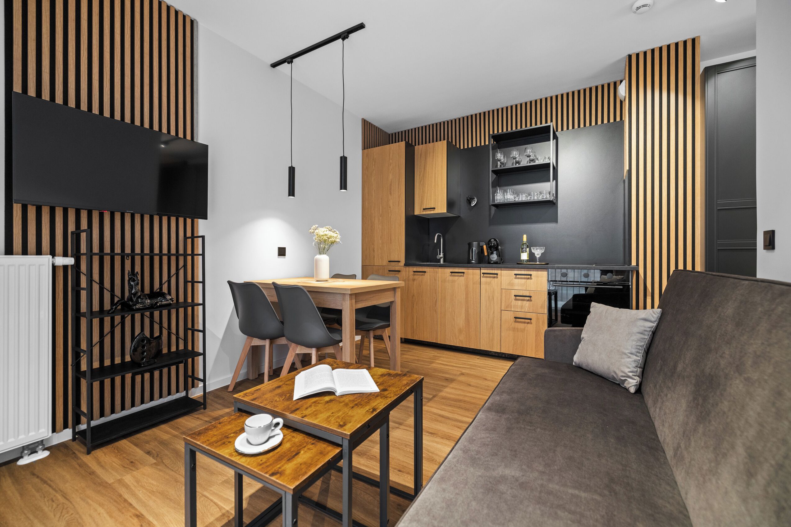 Una cocina moderna con armarios de madera, un área de comedor con una mesa y sillas, y un sofá gris.