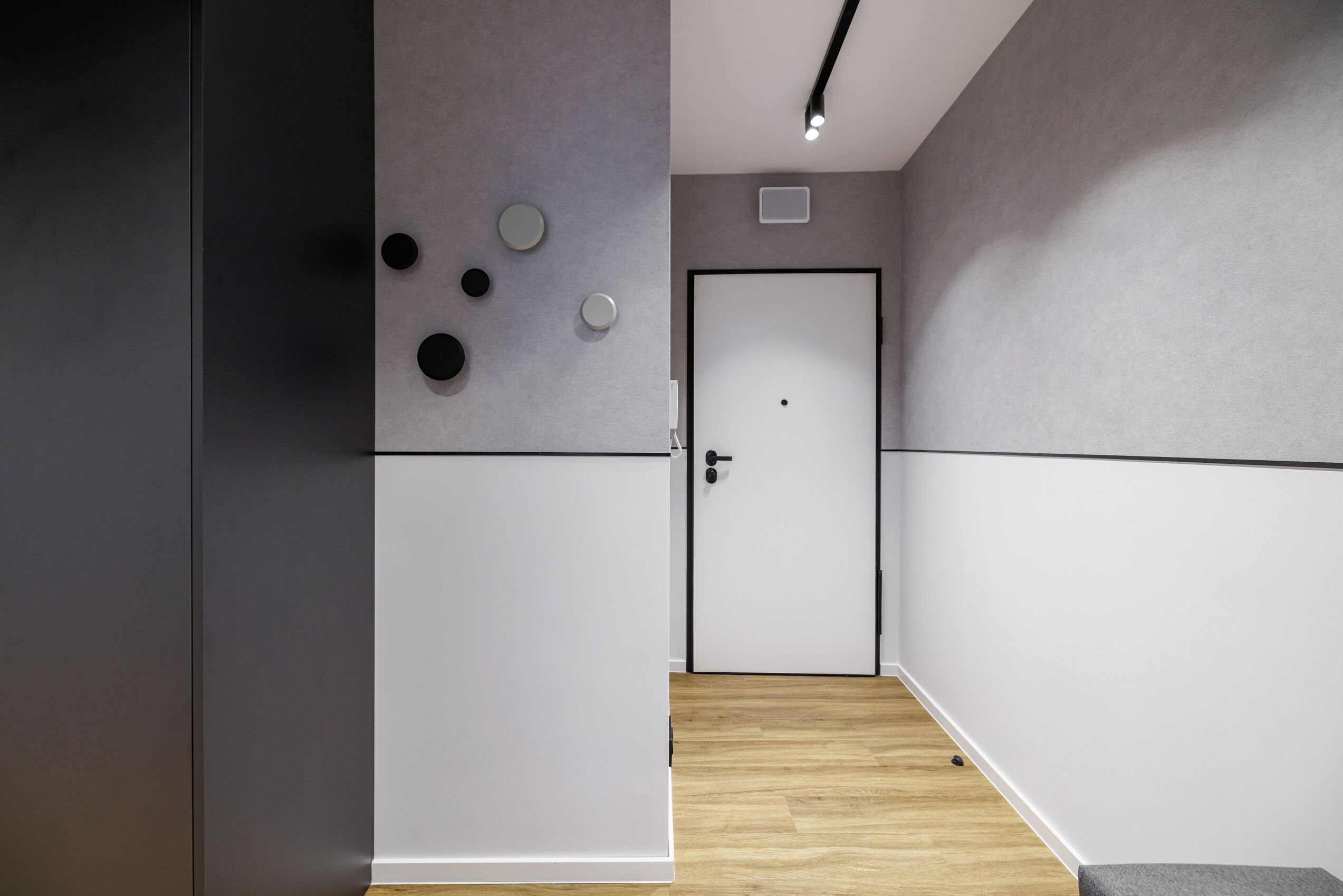 A hallway with a white door, grey walls, and a wooden floor.