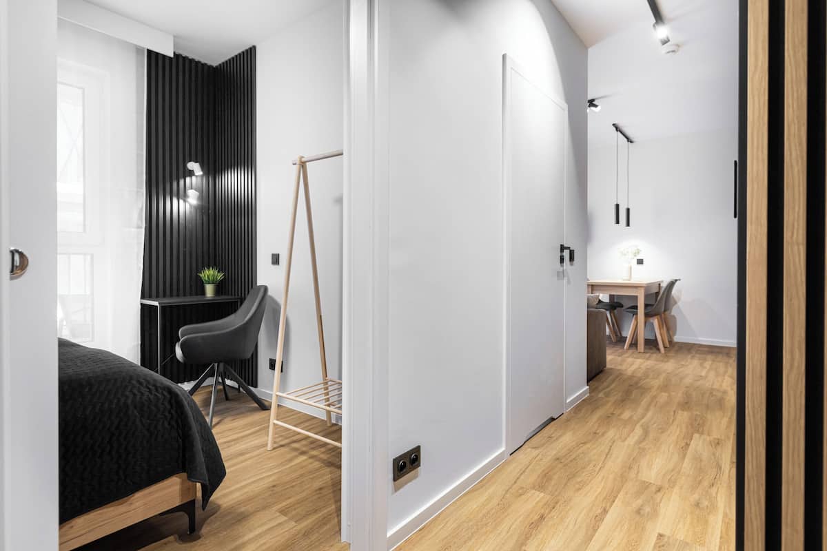 A modern room with a bed, desk, and dining area, featuring a wooden floor and white walls.