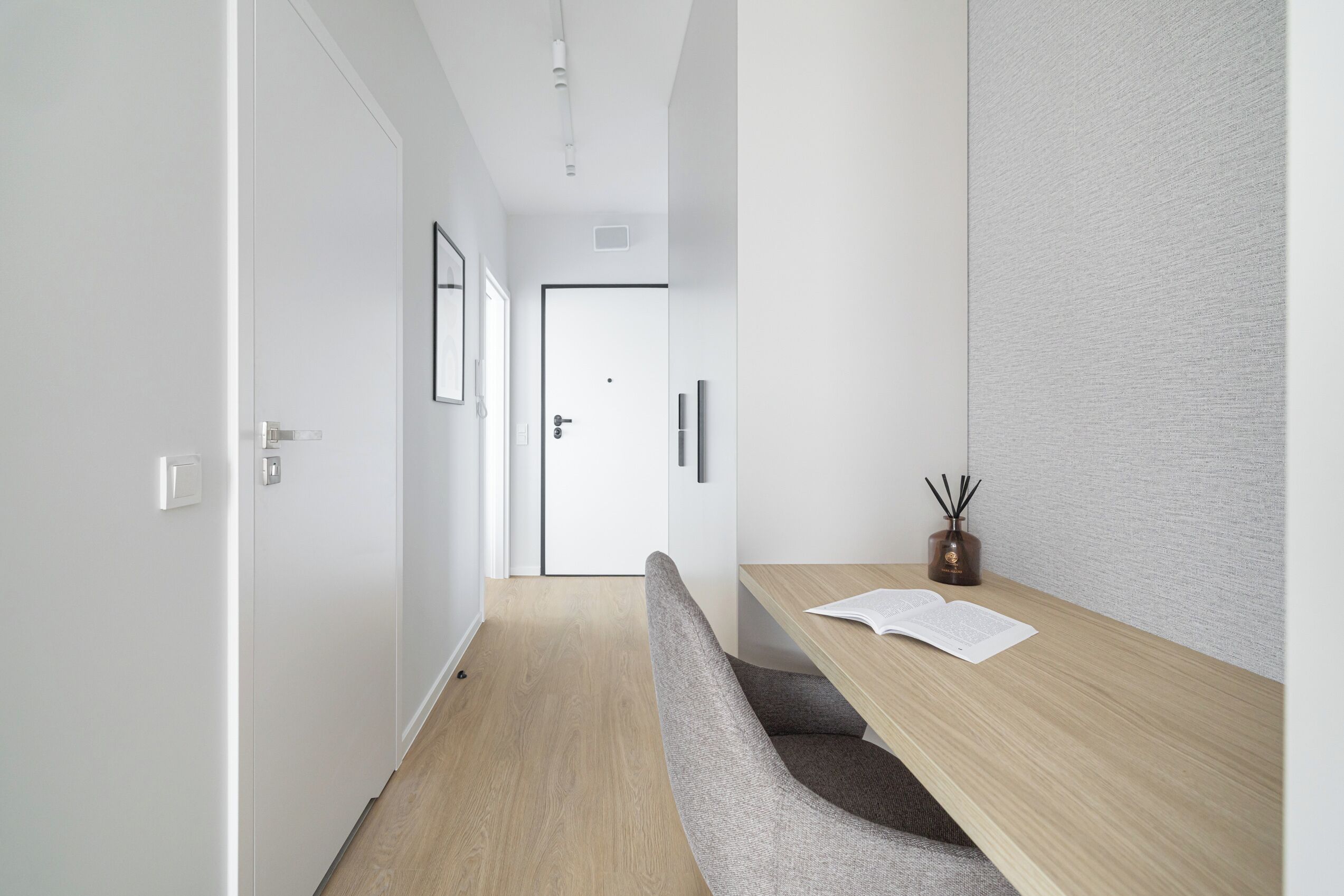 Un couloir moderne avec un plancher en bois, un banc, un bureau avec un livre et une porte au fond.