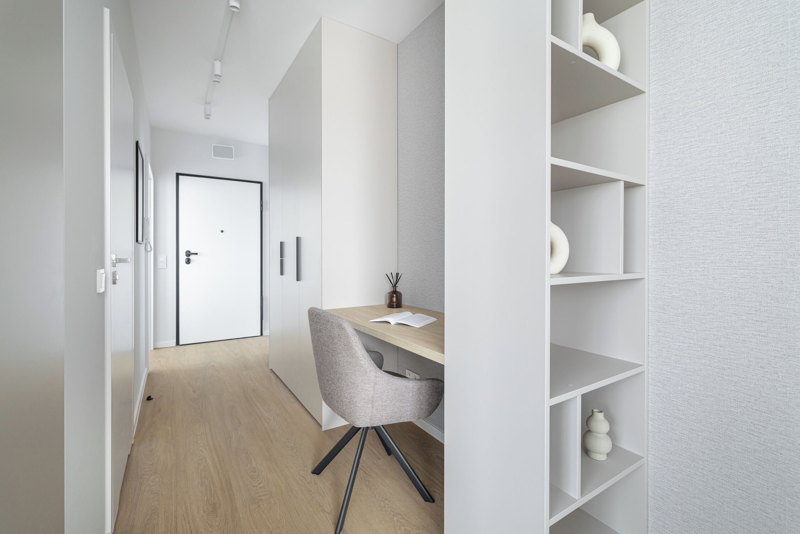 A modern, minimalist office space with a wooden desk, a grey chair, and white shelving units.