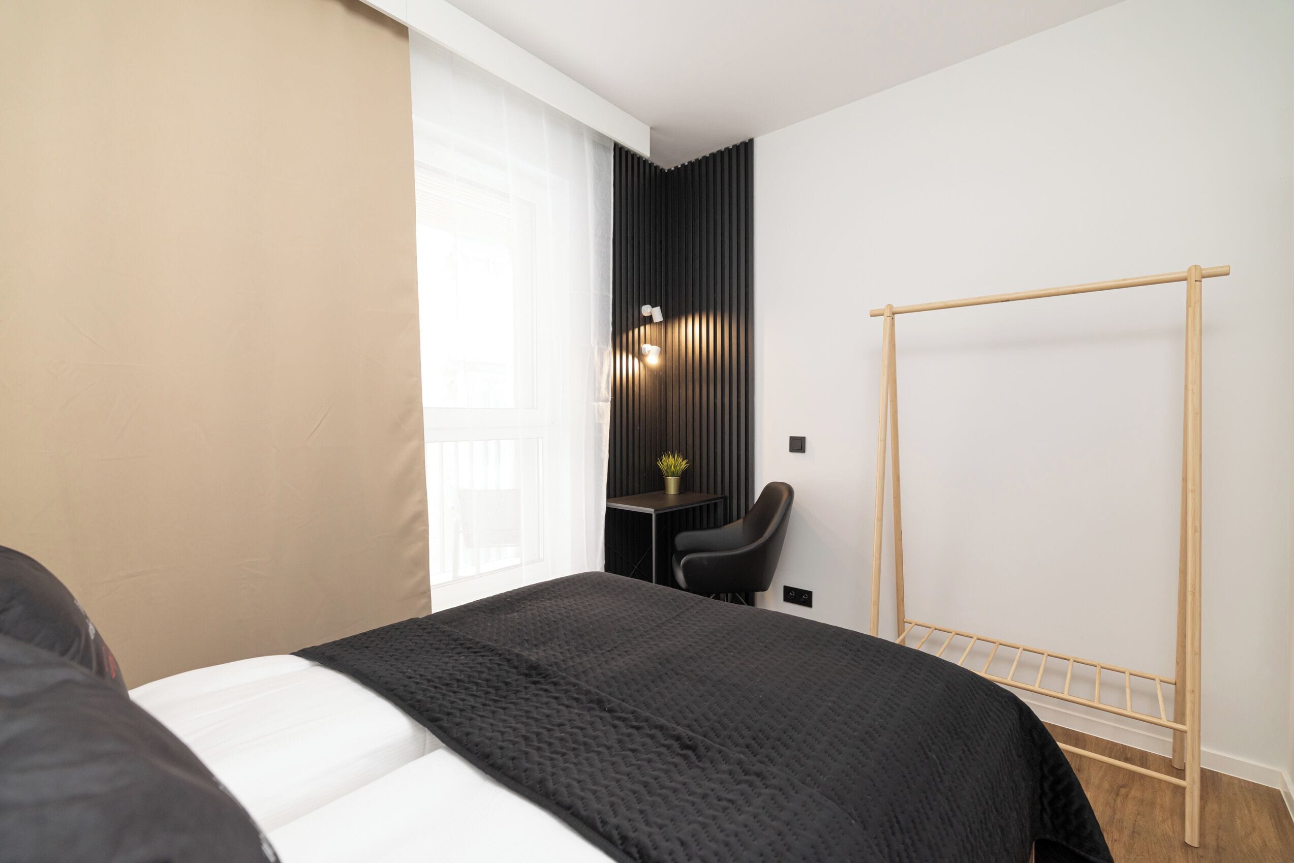 Habitación de hotel con cama, escritorio, silla, un tendedero de madera y una planta en maceta.