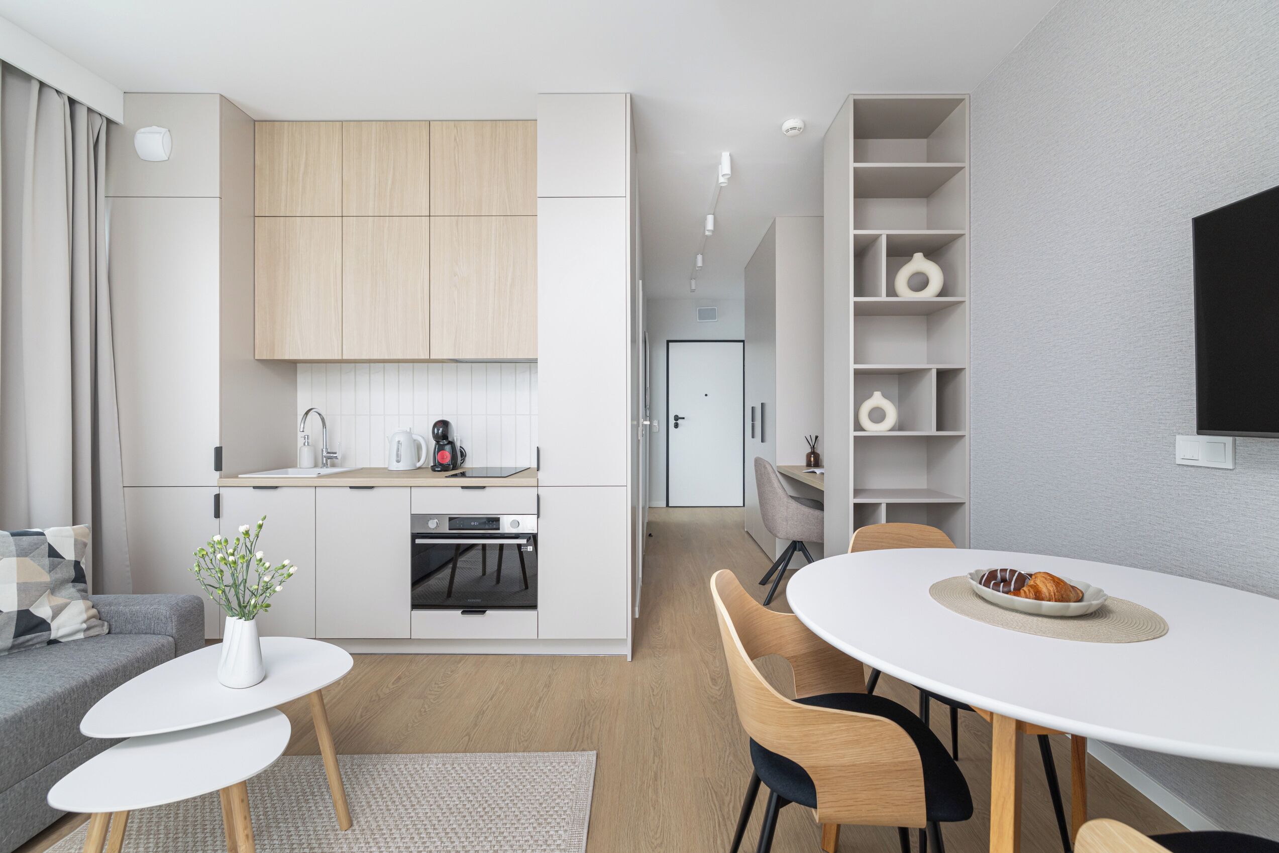 A modern kitchen with white cabinets, a dining area with a white table and chairs, and a grey sofa.