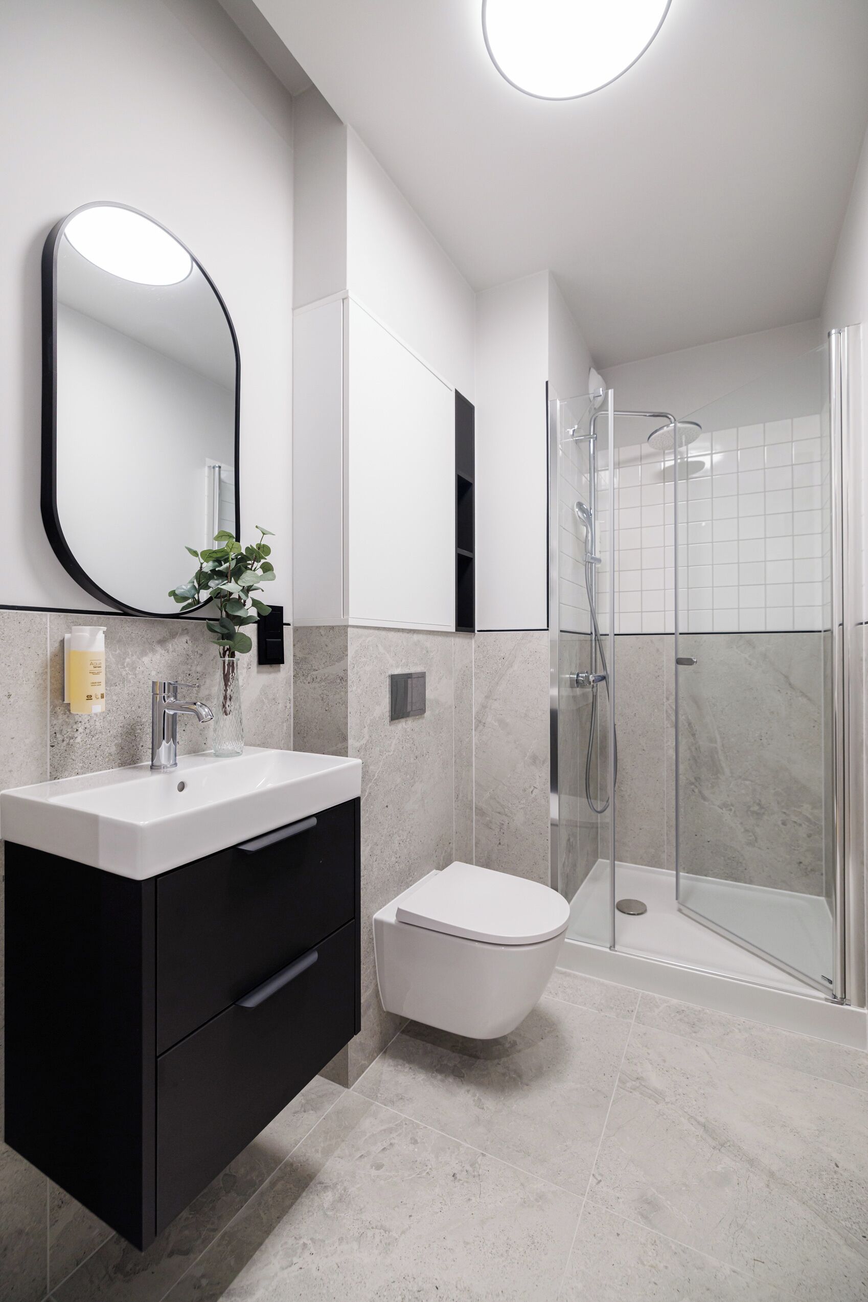 A modern bathroom with a white sink, black cabinet, and a glass shower enclosure.