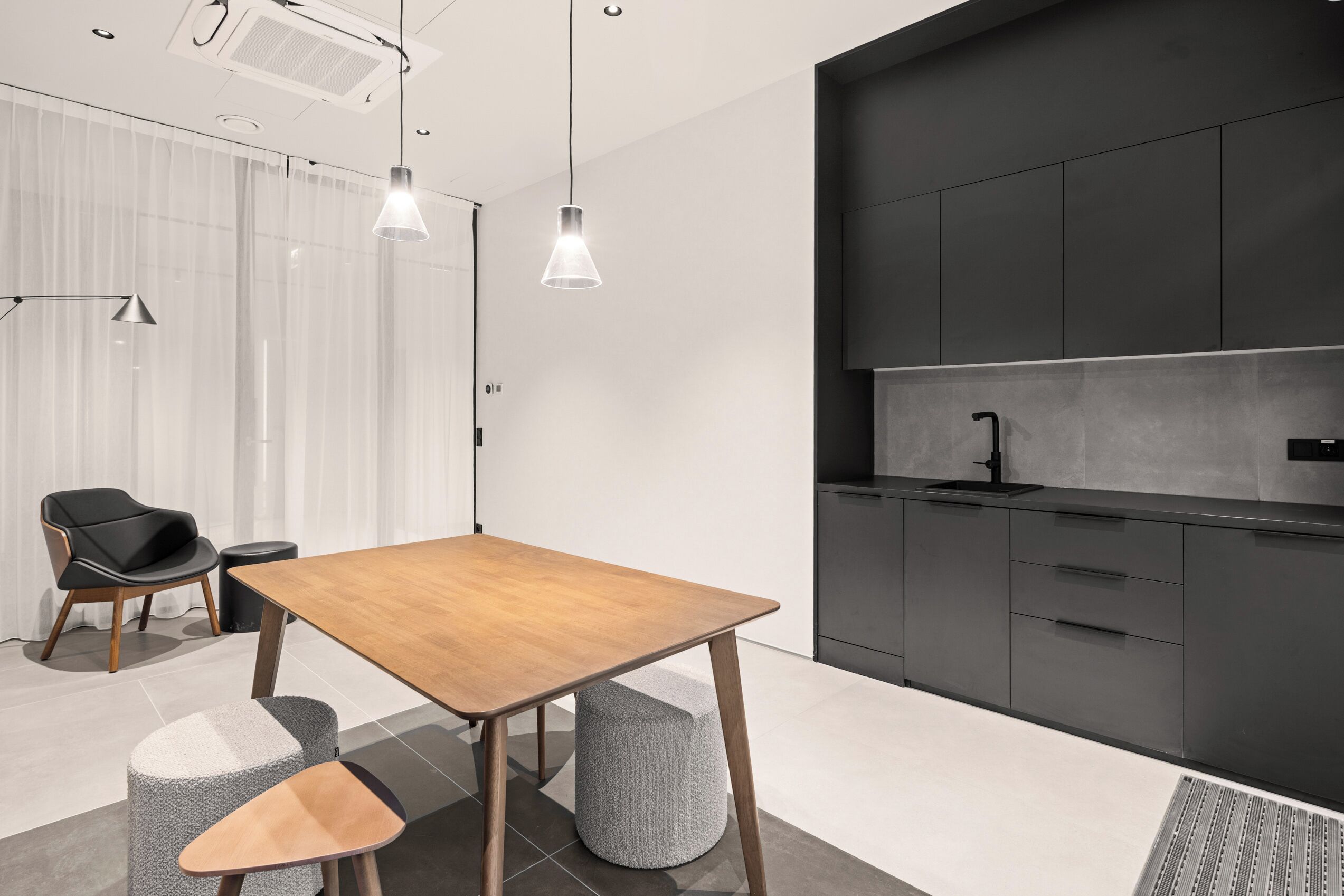 A modern kitchen with dark cabinets, a wooden table, and pendant lighting.