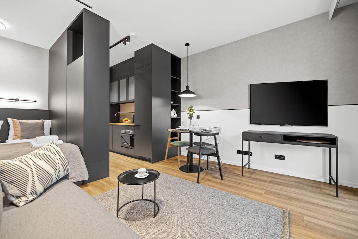 A modern living room with a sofa, a small round table, a TV, and a kitchen area in the background.