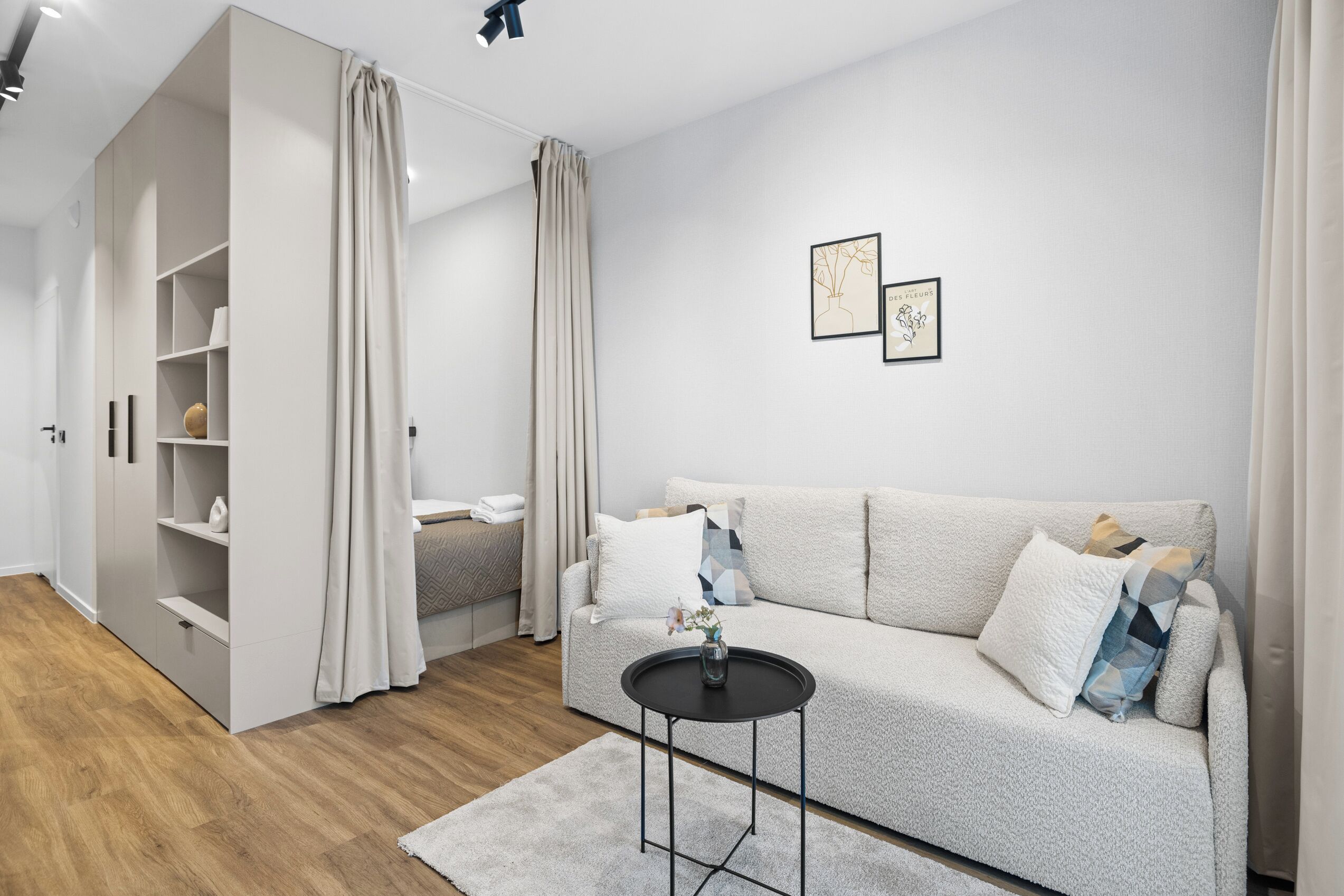 Ein modernes Wohnzimmer mit einer Couch, einem kleinen runden Tisch, einer eingebauten Garderobe und einem Bett mit Kopfteil.