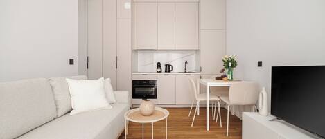 Una sala de estar moderna con sofá, una mesa de comedor con sillas, una zona de cocina con armarios y un televisor sobre un mueble.