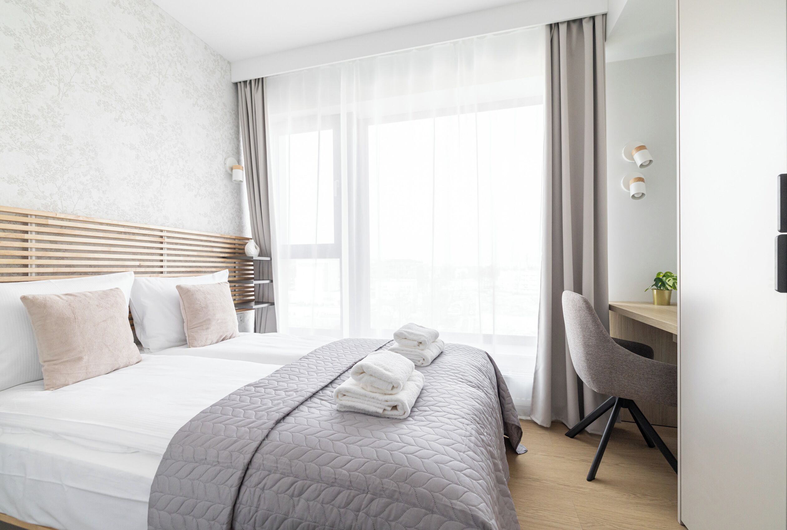 Une chambre d’hôtel moderne avec un grand lit, un bureau et une chaise. Il y a des serviettes sur le lit et une plante sur le bureau.