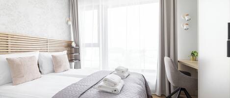 Une chambre d’hôtel moderne avec un grand lit, un bureau et une chaise. Il y a des serviettes sur le lit et une plante sur le bureau.