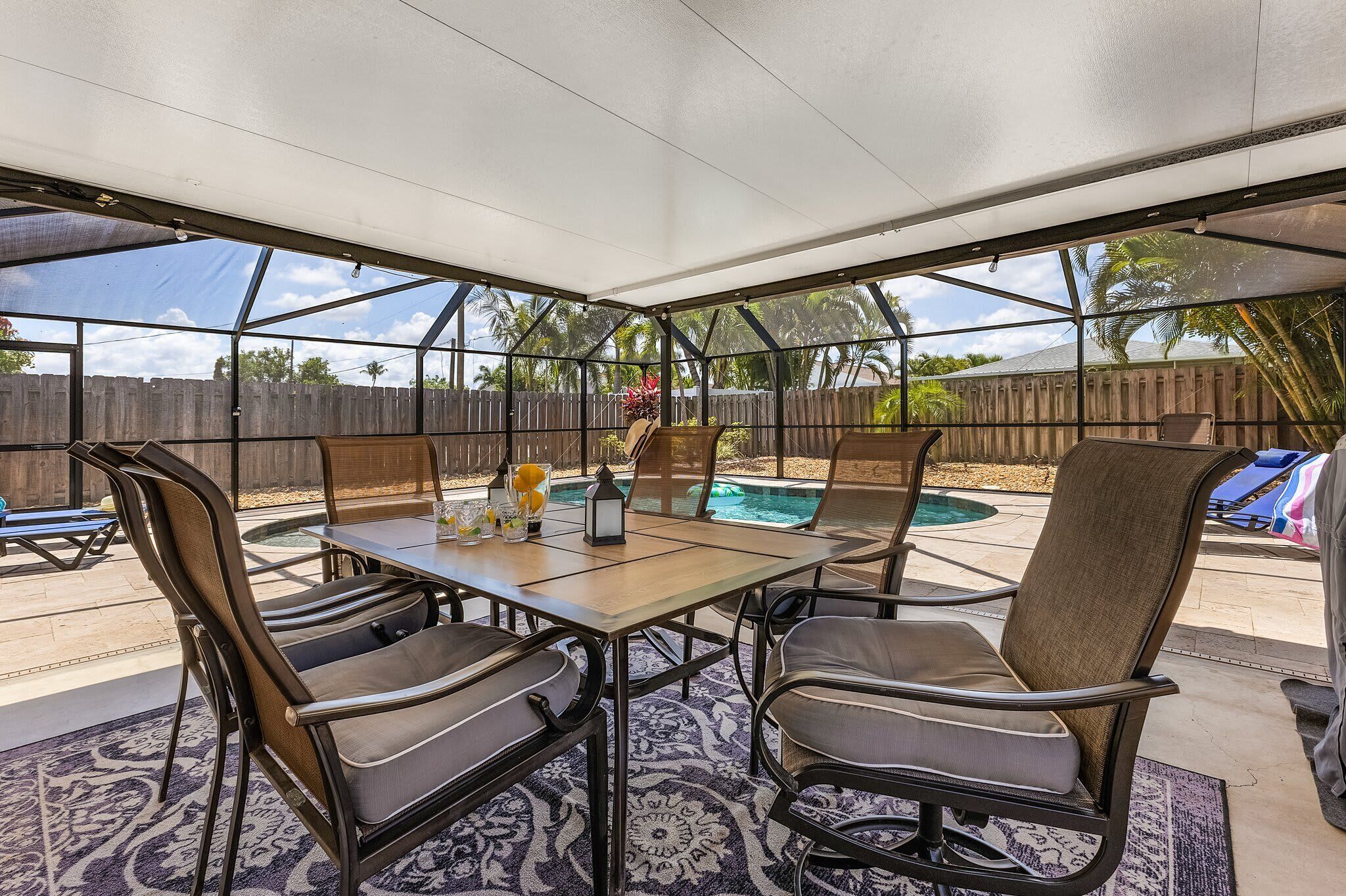 A covered patio with a pool, outdoor seating, and a view of palm trees.
