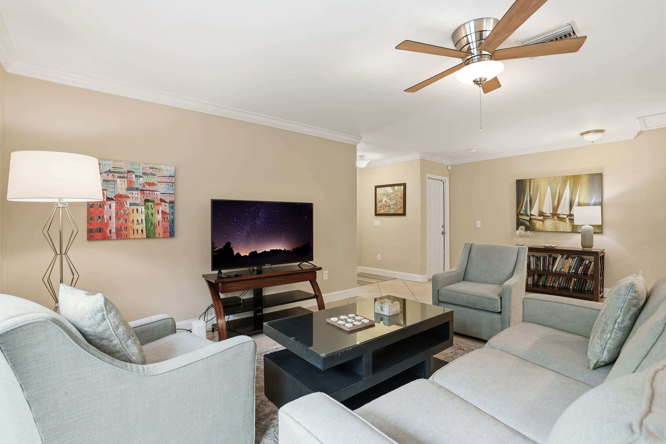 A living room with a flat-screen TV, a ceiling fan, a bookshelf, and a lamp.