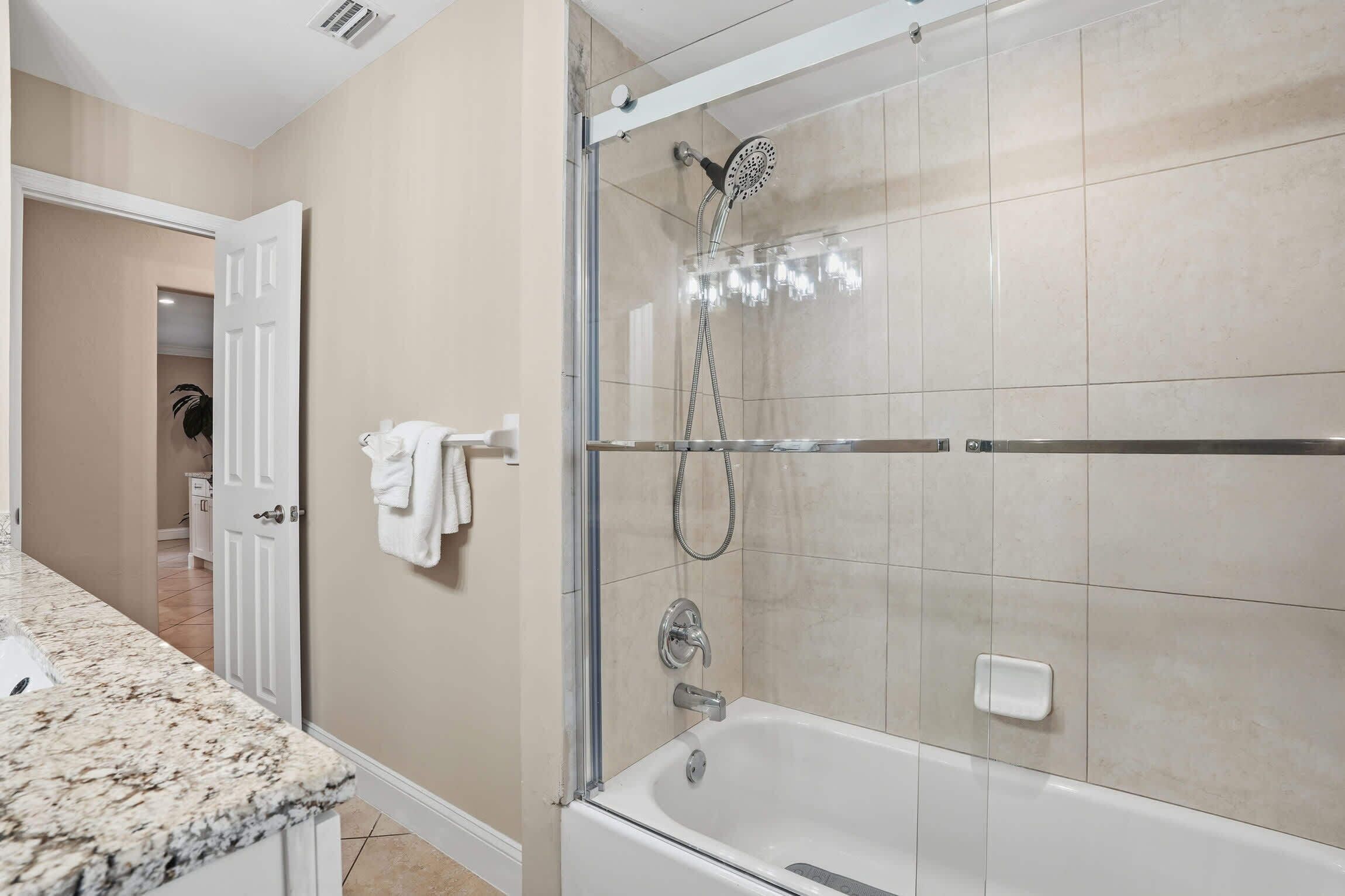 Ein modernes Badezimmer mit einer gläsernen Duschkabine, einer weißen Badewanne und einer Marmorarbeitsplatte.