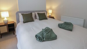 A neatly made bed with green towels, two bedside lamps, and a radiator. - Cariad Cottage (Hereford)