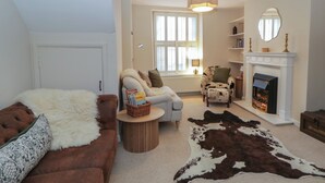 A cozy living room with a fireplace, a sofa, a chair, and a cowhide rug. - Cariad Cottage (Hereford)