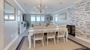 Uma sala de jantar espaçosa com uma mesa grande e cadeiras, um candelabro e uma parede de lareira em pedra.