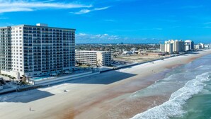 Um hotel à beira-mar com vários edifícios altos, uma praia de areia e um céu azul límpido.