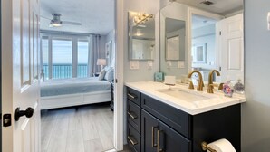Quarto moderno com varanda, um espelho grande e banheiro com toucador e pias duplas.
