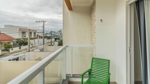 Ein Balkon mit einem grünen Stuhl, einem weißen Geländer und Blick auf Nachbarhäuser.