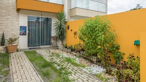 Ein modernes Gebäude mit gelber Fassade, einem Glastür-Eingang und einem kleinen Gartenbereich mit Pflanzkübeln und einem Weg.