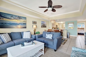 Ein Wohnzimmer mit grauem Ecksofa, einem weißen Couchtisch und einem Deckenventilator.
