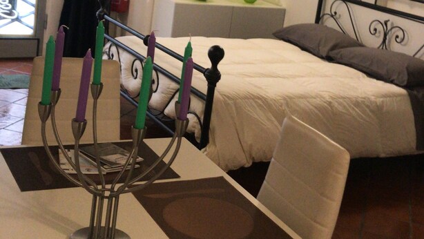 Une pièce avec un lit, une table avec des bougies, une fenêtre avec des rideaux et une horloge murale.