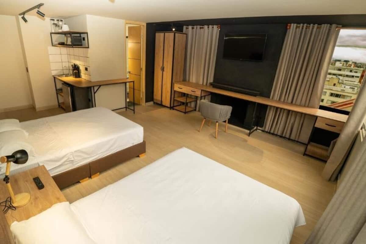 Een hotelkamer met twee bedden, een bureau, een stoel, een televisie en uitzicht op de stad.