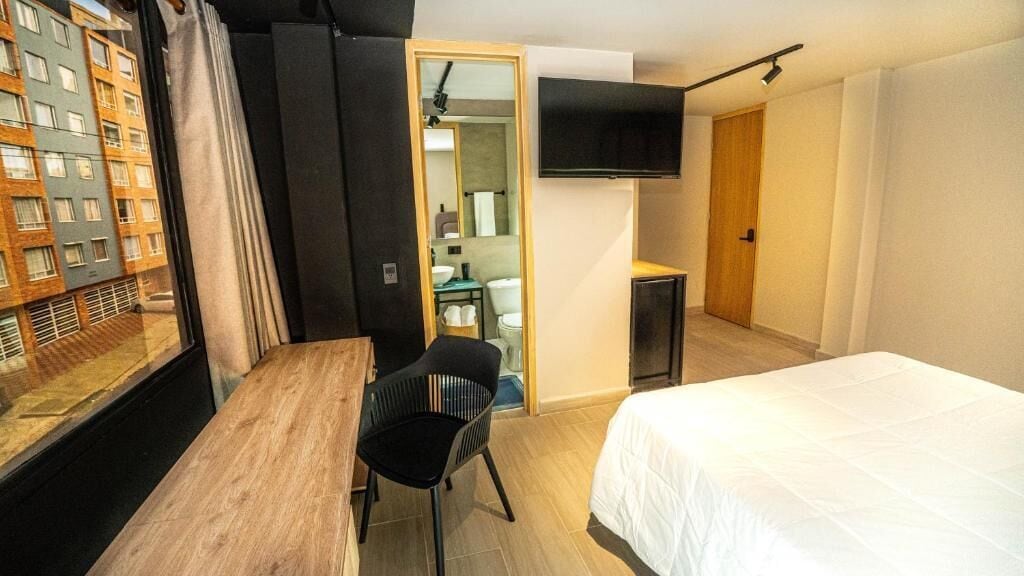 Una habitació d'hotel amb un llit, una taula de treball, una cadira, un televisor i vista a un edifici a l'exterior.