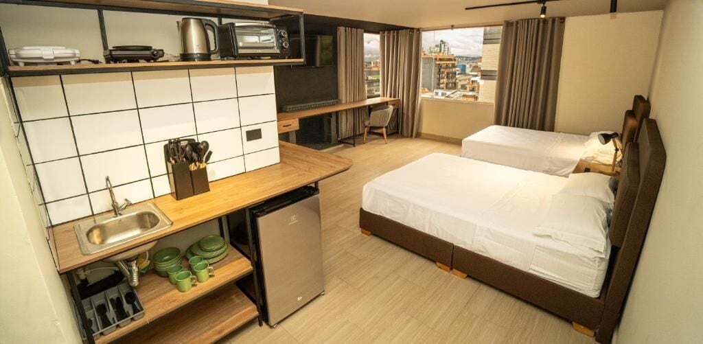 Quarto de hotel com cozinha compacta, uma cama, uma escrivaninha e vista para a cidade.