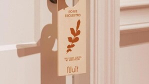 A door with a brass handle and a tag hanging on it. The tag has text and a leaf design. - Hotel Nuit by ilar (Bogotá)