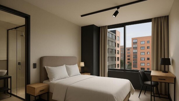 A modern hotel room with a large bed, a desk, a chair, a small table, a lamp, and a view of the city through the window. - Hotel Nuit by ilar (Bogotá)