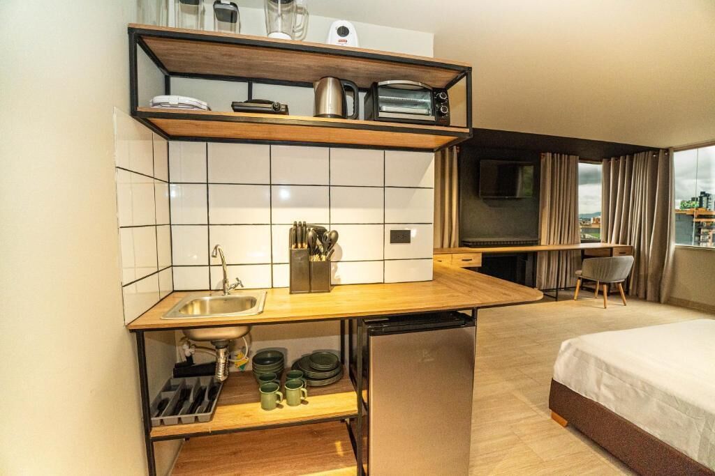 A compact hotel room with a kitchenette, a bed, a TV, and a view of the cityscape.