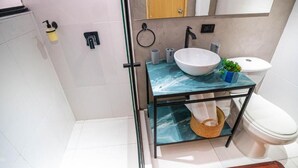 A modern bathroom with a glass vanity, a white sink, a toilet, and a shower area. - Hotel Nuit by ilar (Bogotá)