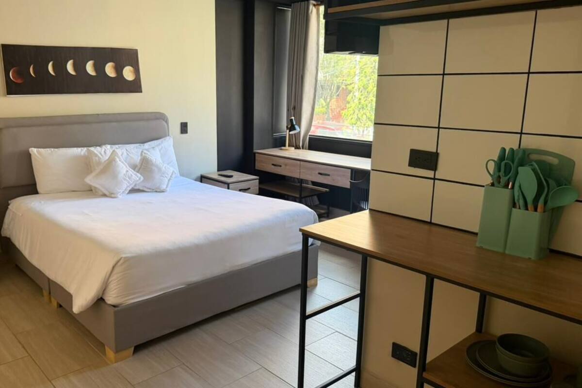 Een slaapkamer met een bed, een bureau, een raam en een kunstwerk aan de muur.