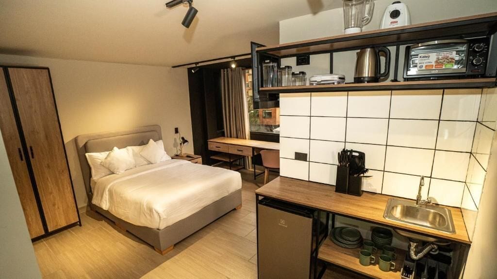 Une chambre d’hôtel de taille réduite, comprenant un lit, une petite kitchenette et un bureau.