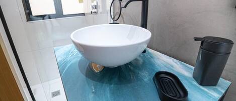 A bathroom with a white vessel sink, a black trash bin, and a blue marble countertop.