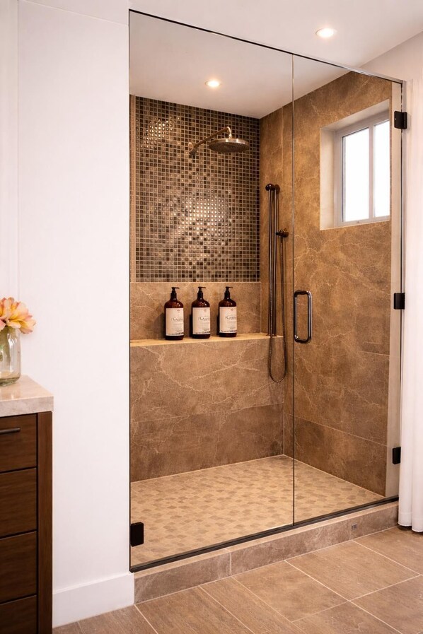 A glass-enclosed shower with a tiled wall, a shelf with bottles, and a window. - SED DE VALLE-VALLE DE GUADALUPE  (Valle de Guadalupe)