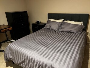 Ein ordentlich bezogenes Bett mit Streifenmuster, ein dunkles Kopfteil und ein Nachttischchen mit einer Lampe.
