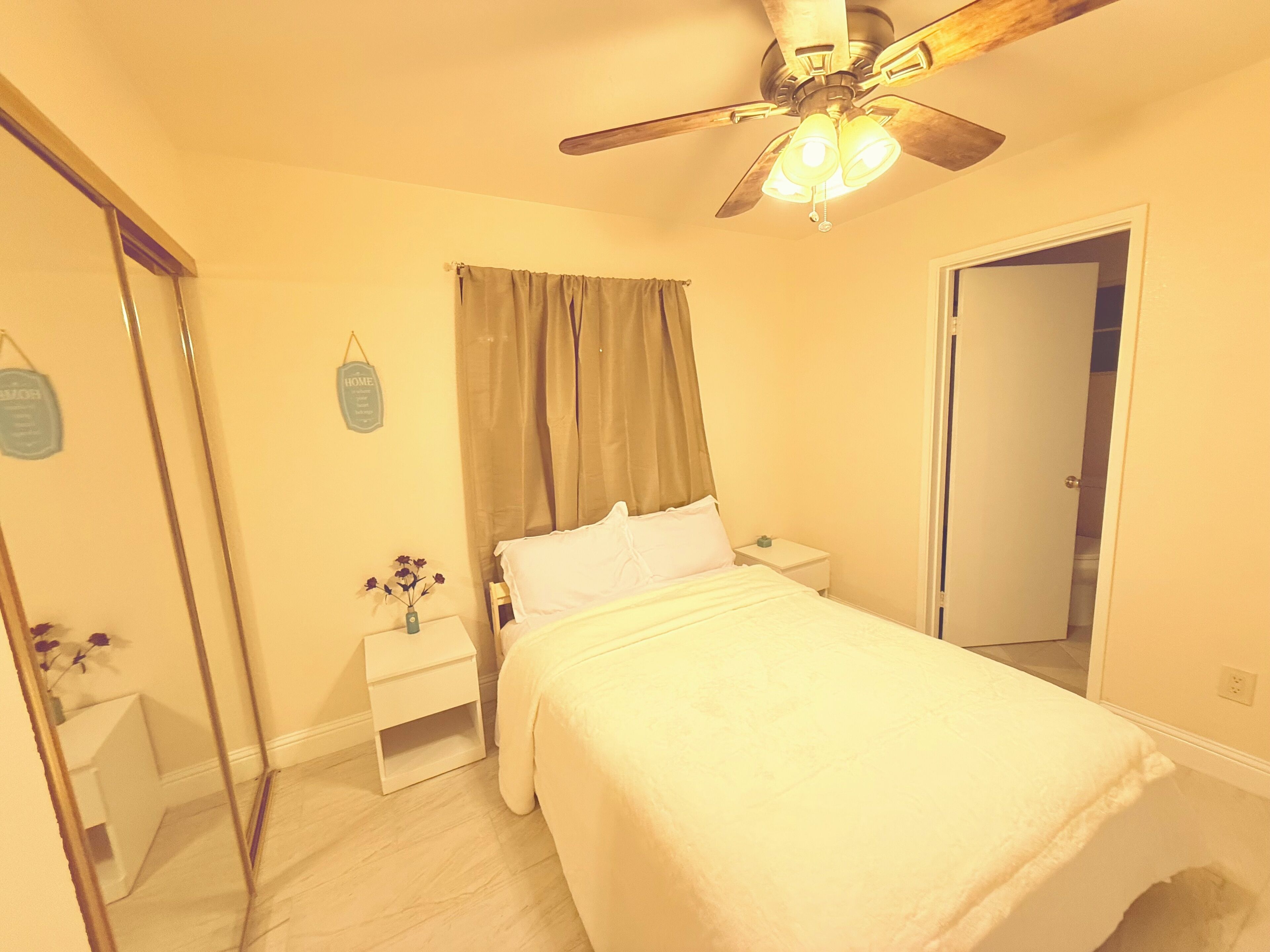 Un dormitorio con cama, mesita de noche, espejo, ventilador de techo y puerta.