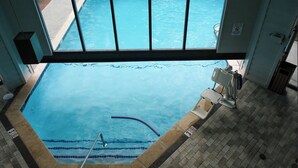Ein Hallenbad mit klarem Wasser, einem Sprungbrett und einem Rettungsschwimmerstuhl.