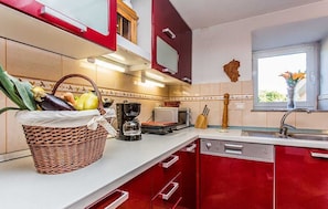 A kitchen with red cabinets, a coffee maker, a toaster, and a basket of vegetables. - Holiday house KRAS with spacious garden (Kras)