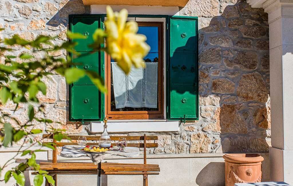 A stone building with a wooden table and a window with green shutters.