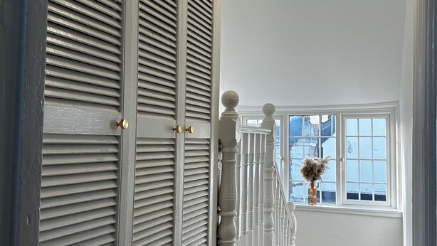 A hallway with a carpeted floor, a white railing, and a window with a view of the outside. - Charming 4-bedroom apartment in lively London neighborhood (London)