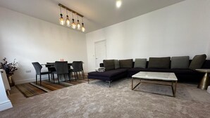 A modern living room with a sectional sofa, a coffee table, a dining area with chairs, and a hanging light fixture. - Charming 4-bedroom apartment in lively London neighborhood (London)