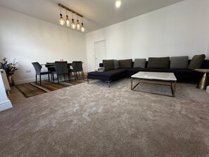 Una sala de estar moderna con un sofá seccional, una mesa de centro, un comedor con sillas y una lámpara colgante.