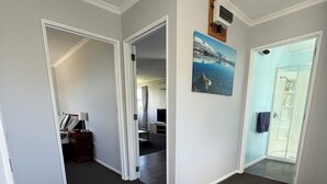 En hotellkorridor med mörkt heltäckningsmatta, vita väggar och en målning som föreställer ett kustlandskap.