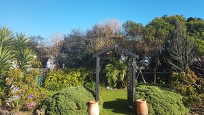 En trädgård med en pergola av trä, krukväxter och en klarblå himmel.