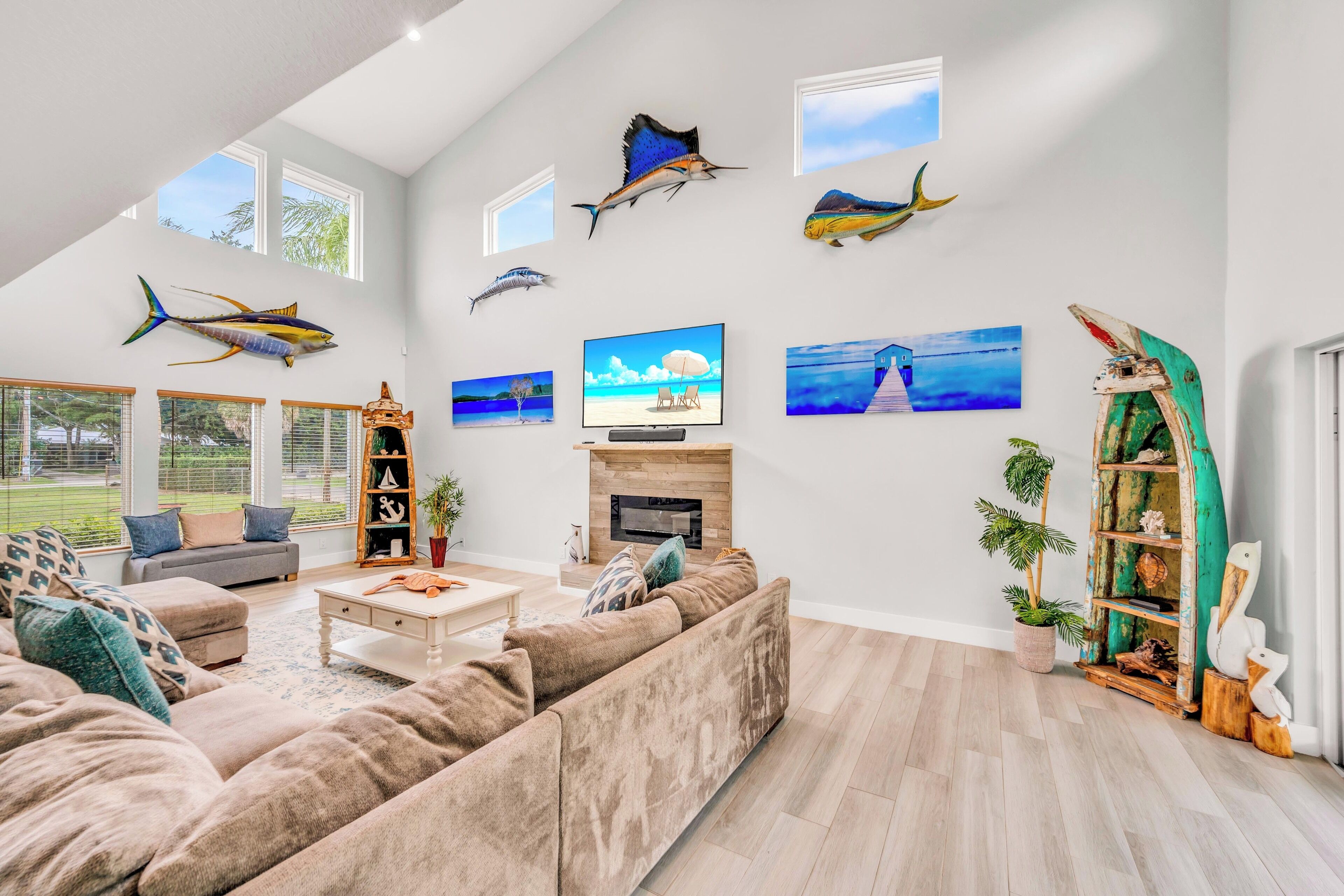 Un salon spacieux avec un grand canapé, une cheminée et des œuvres d’art accrochées au mur, représentant notamment des poissons et des scènes de plage.