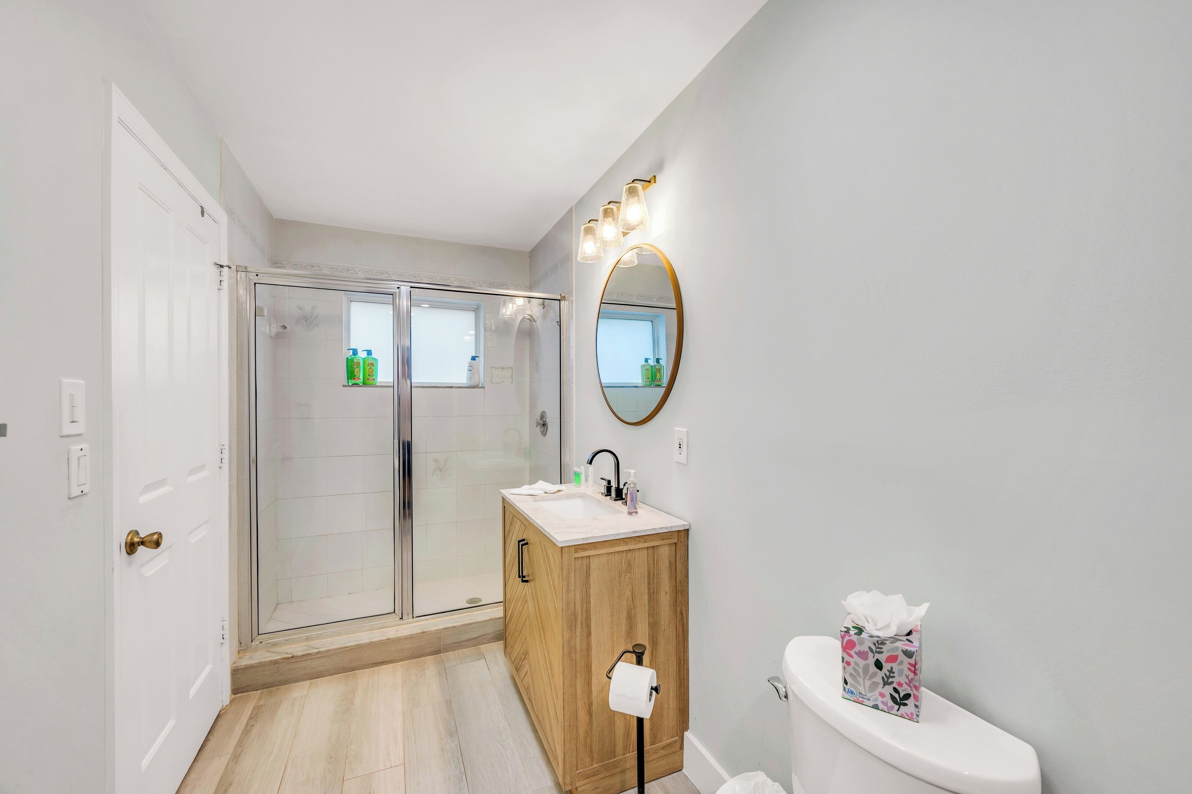 Ein modernes Badezimmer mit Duschkabine aus Glas, einem Holzkosmetikschrank mit Waschbecken und einer Toilette.