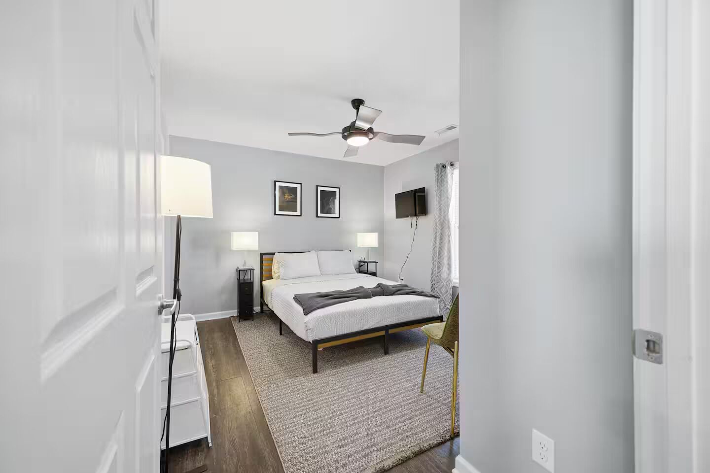 A bedroom with a bed, bedside tables, a ceiling fan, and a TV on the wall.